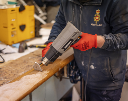Another look at hands holding a heat gun to remove varnish from a handrail. 