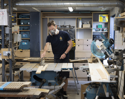 In the workshop, a maintenance man is cutting a template for mending deck planks. 
