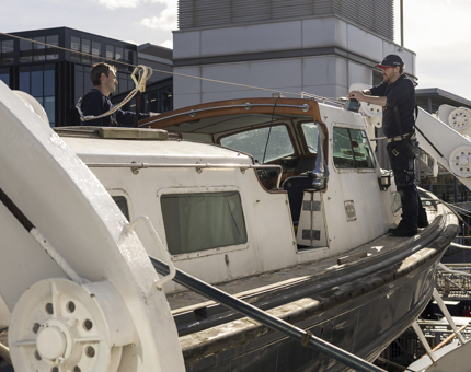 Two Maintenance men working on the Fast Motor Launch suspended alongside Britannia in the Port of Leith. 