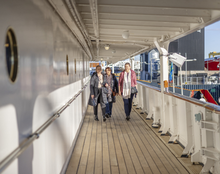 Three visitors are walking along Britannia's decks in Leith. 