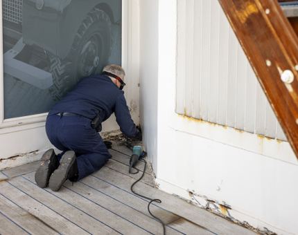A man is crouching down, preparing a wall to be painted.