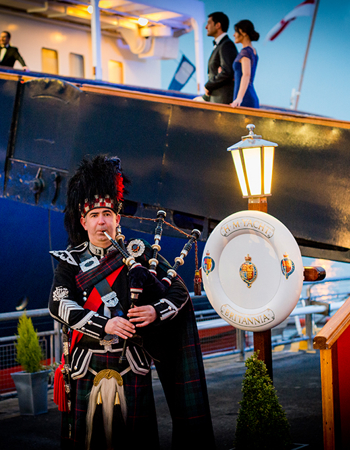 A piper in traditional dress stands at The Royal Yacht Britannia's Royal Brow. 