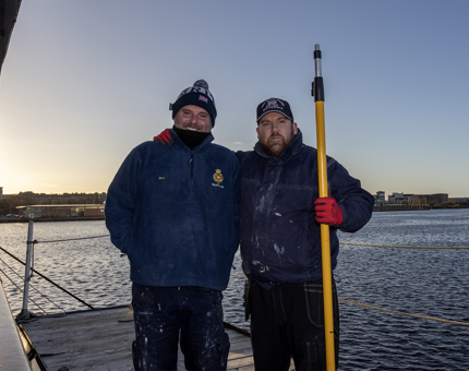 Two Maintenance Team members standing smiling as they pause in painting the outside of Britannia. 