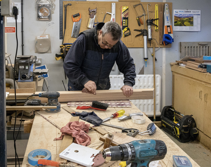 A man from the Maintenance Team sanding a wooden leg for a lectern. 