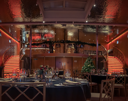 Round tables set for dinner in Fingal's Ballroom. There is a Christmas tree on the right and a mezzanine level containing a Bar. 