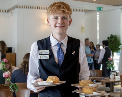 A Waiter in the Tearoom carrying plates of scones to visitors. 
