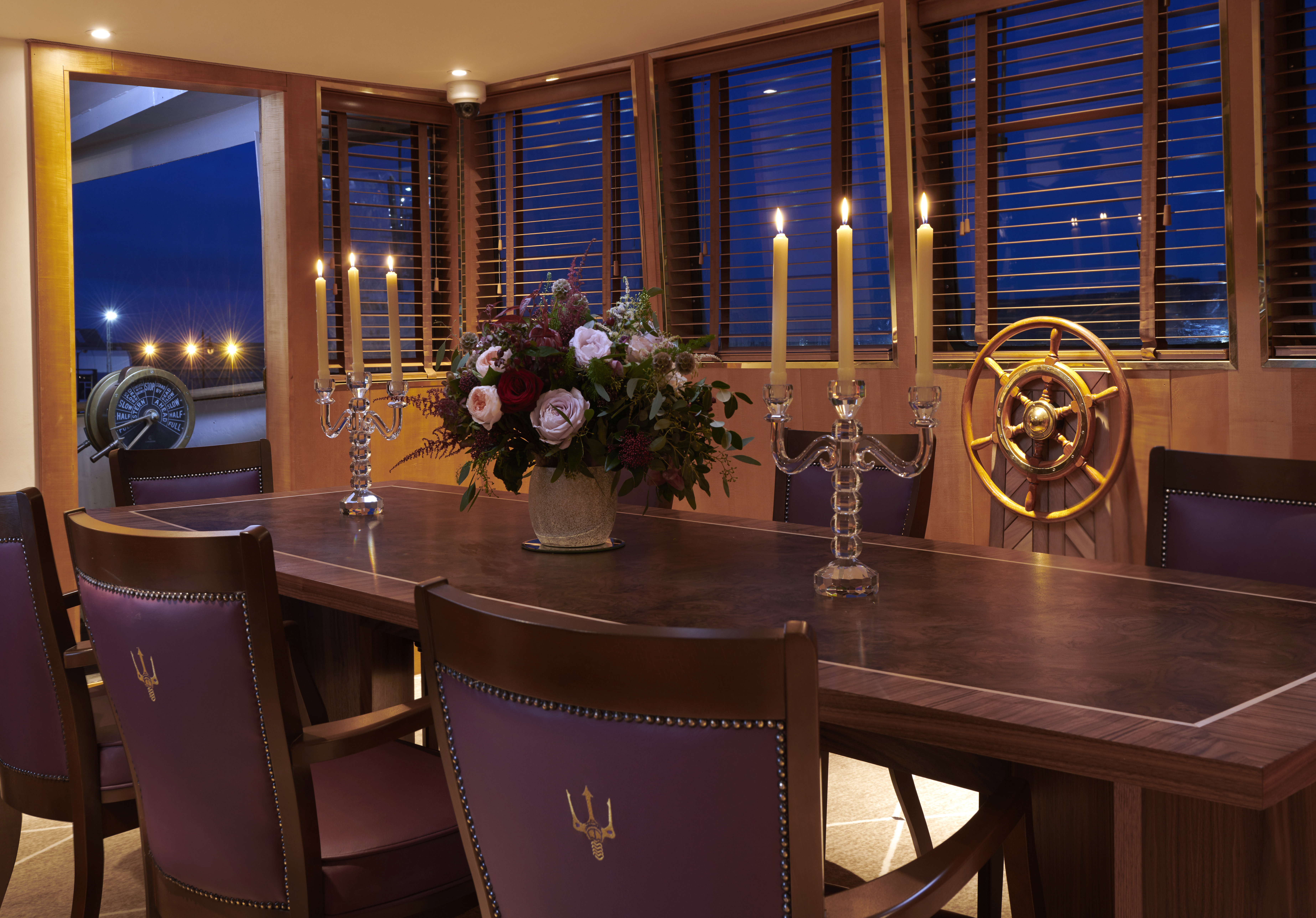 The Bridge of Fingal with a large dining table and chairs. There are candelabra on the table and the ship's wheel is in the background.