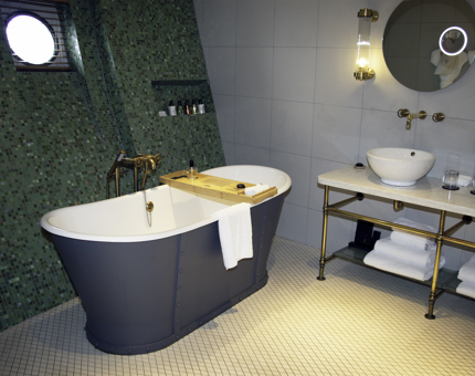 A bathroom in a Fingal cabin with a free-standing bathtub and wash basin. The walls have green mosaic tiles. 