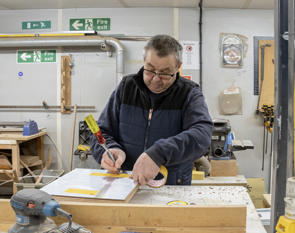 A man from the Maintenance team applying tape to the reverse of a sign in the workshop. 