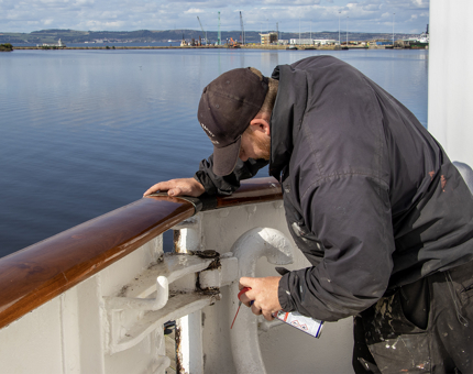 A member of the Maintenance team adjusting a hinge on a gate on the Fo's'cle deck. 