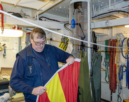 A man from Maintenance holding a red and yellow flag as he pulls the flags onto a rope. 