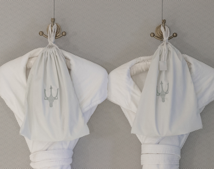 Two fluffy dressing gowns hanging on hangers with bags containing slippers. 