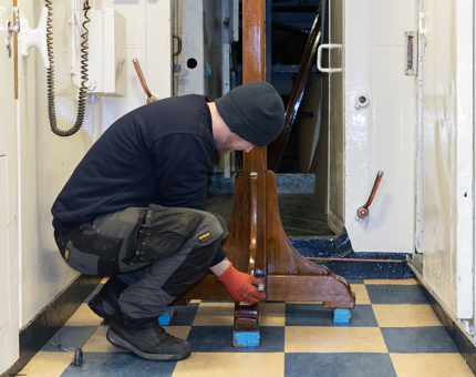 A Maintenance Assistant painting varnish onto a wooden stand. 