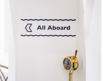 Blue and white signage 'All aboard' on the wall and a brass engine order telegraph. 