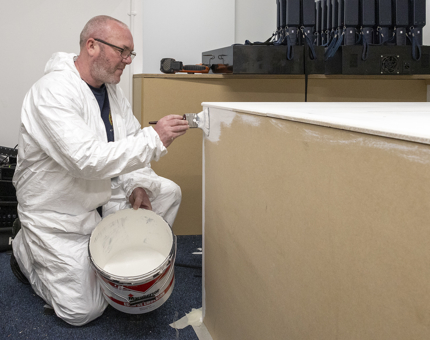 A man painting the wooden handset are with white paint. 
