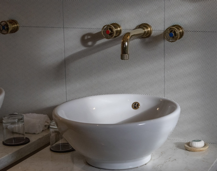 A round wash basin inside a cabin bathroom. There are nautical-inspired brass tap fittings. 