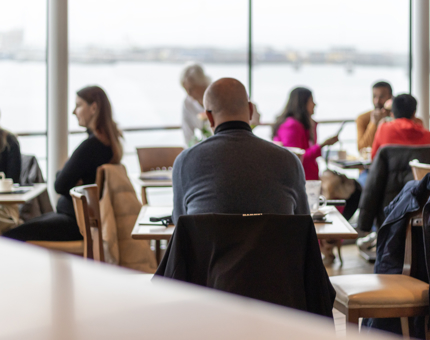 The Royal Deck Tearoom where visitors are sitting at different tables. The view from the window is of the waterside. 
