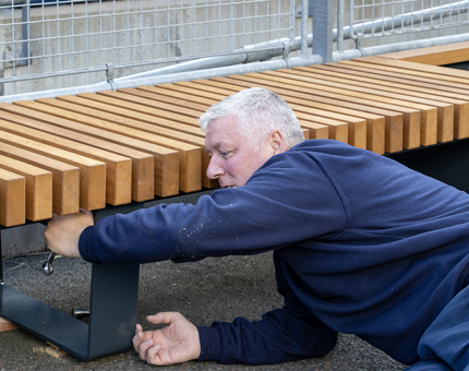A man from the Facilities team assembling a wooden bench. 
