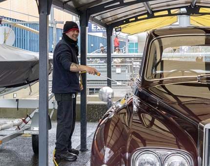 A member of the Facilities team hosing the Rolls-Royce car which is in the garage on the Quayside. 