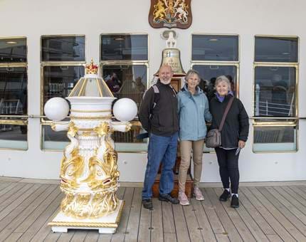 A man and two women stand posing for a photo next to the Bell and compass Binnacle. 