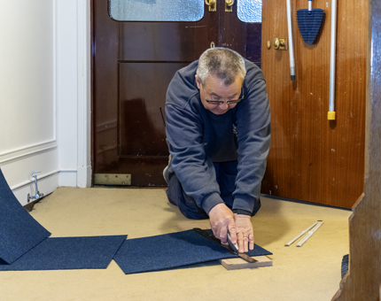 A man cutting carpet into tile shapes