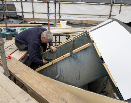 A man working on the drainage system at the top of the funnel on The Royal Yacht Britannia