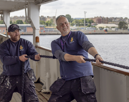 Two men from Maintenance are pulling the rope of the paint cat. 