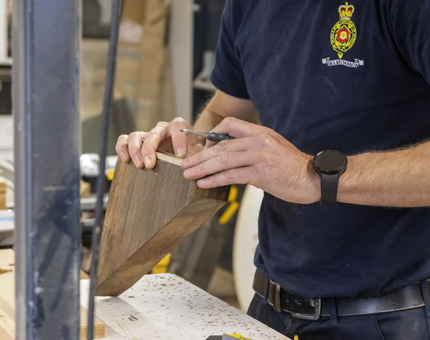 An up-close look as a man is holding a piece of wood with a screwdriver. 