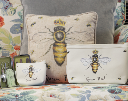 A selection of gifts with a bee illustration including a cushion, make up bag, purse and manicure set. 