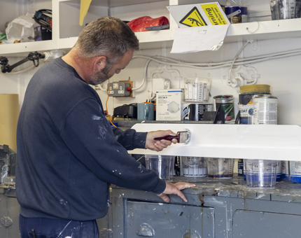 A man from Maintenance painting wood in the Workshop. 