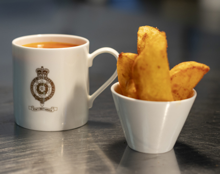 A mug of soup and a bowl of potato wedges. 