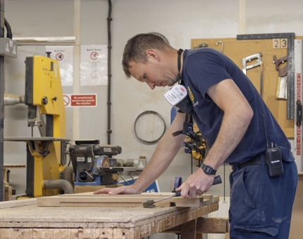 A man in a workshop making a storage container from wood. 