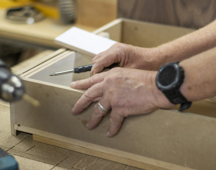 A close up of hands holding a screwdriver making a drawer. 