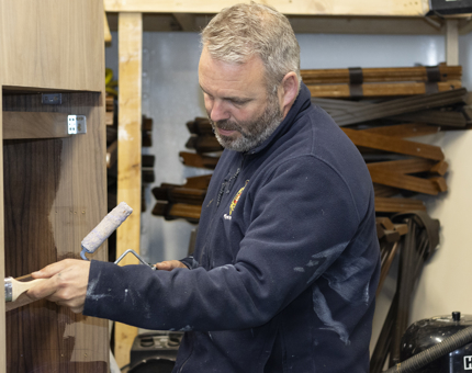 A man holding a paintbrush varnishing a podium. 