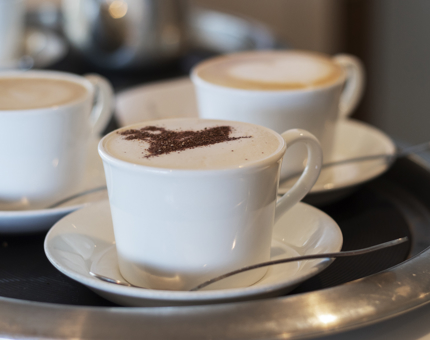 A tray of coffees with a chocolate stencil of a ship on them. 