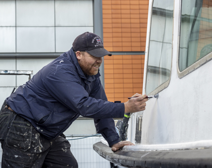 A man painting the side of a boat. 