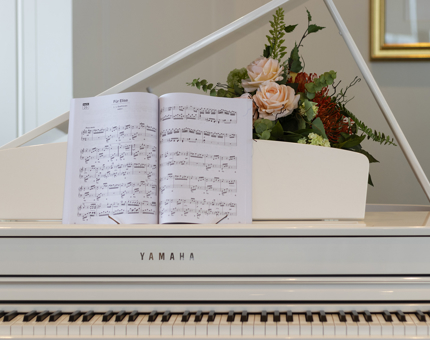 A close-up of a white grand piano with sheet music and a bunch of flowers. 