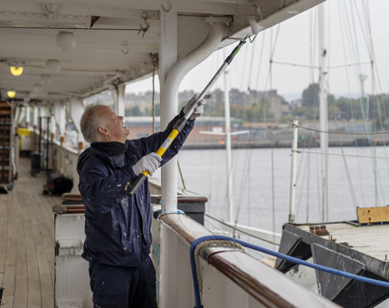 A man with a paint roller painting part of the Starboard side of the ships walkway covering white.