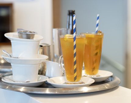 A silver tray with two iced teas and two tea cups on it. 