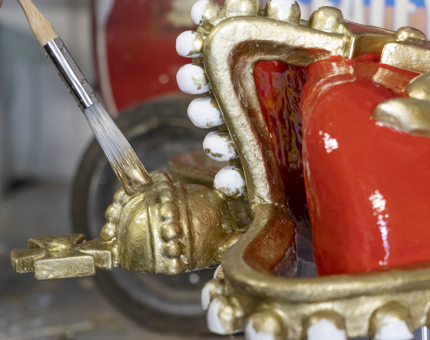 A close up of a crown mold being painted with gold paint. 
