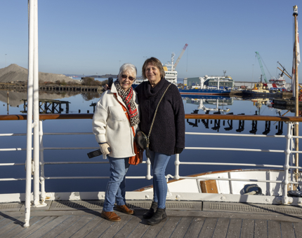 Two women posing for a photo in the sunshine on the Verandah Deck. 