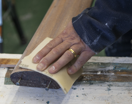 A close-up of a hand sanding a handrail. 