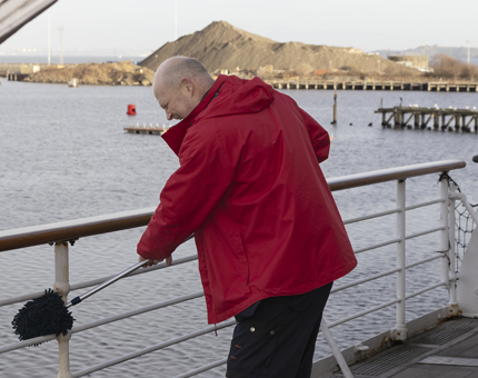 A member of the Housekeeping team is polishing railings on the starboard side. 