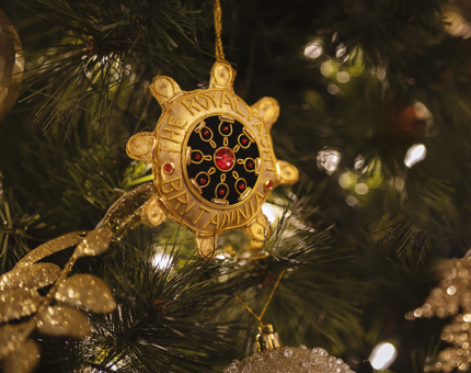 A gold Christmas tree ornament shaped like a ship's wheel. 