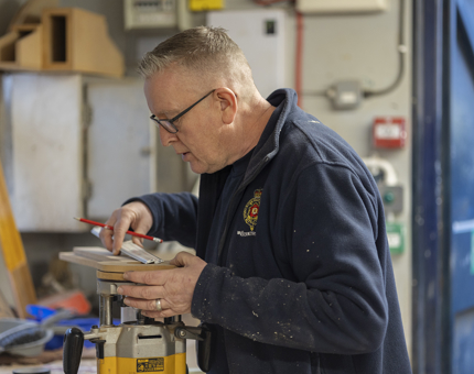 Maintenance team member, Mark, holding a pencil and ruler and setting up a router to make light inserts. 