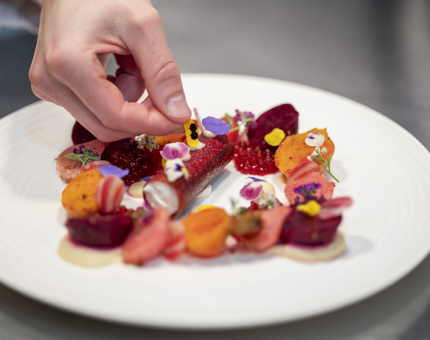 A hand places garnishes on a beetroot started dish. 