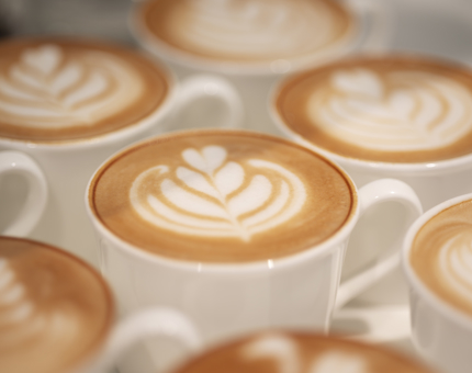 A close up of seven coffees with leaf-style coffee art. 