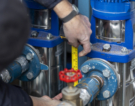 A man using a yellow tape measure to measure pipes on a water pump. 