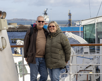 A man and a woman posing for a photo on the Bridge of Britannia. Behind them is a view over the water. 