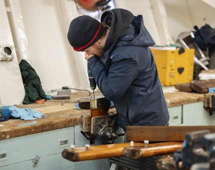 A man is holding a drill, removing brass ends on a handrail. 